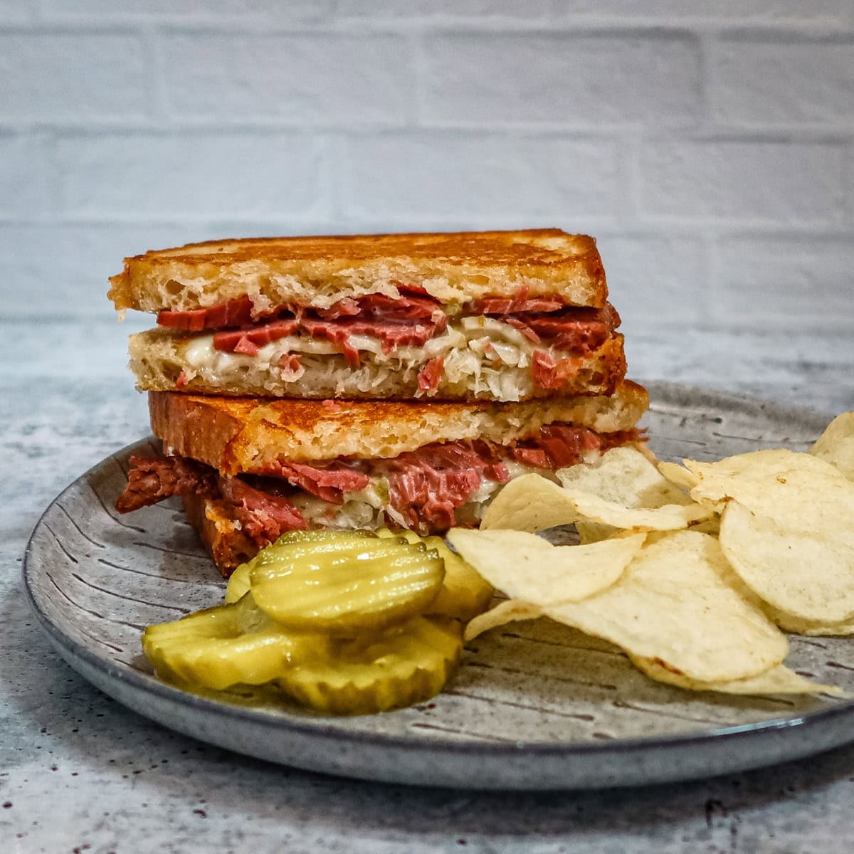 A reuben sandwich on a plate with chips and pickles.