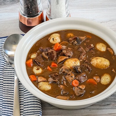 A bowl of beef Burgundy stew with baby potatoes, mushrooms, carrots, and beef cubes.