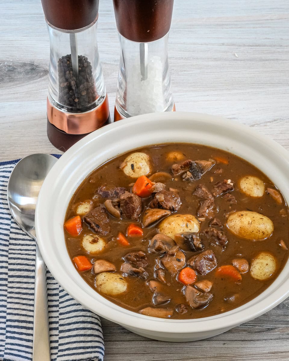 A bowl of beef Burgundy stew with baby potatoes, mushrooms, carrots, and beef cubes.