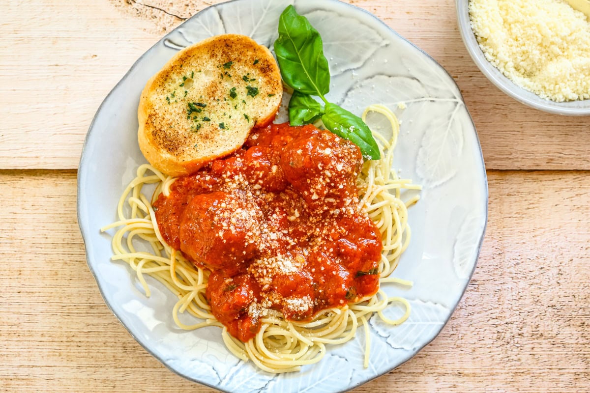 A plate of spaghetti with meatballs and sauce, and a slice of garlic bread.