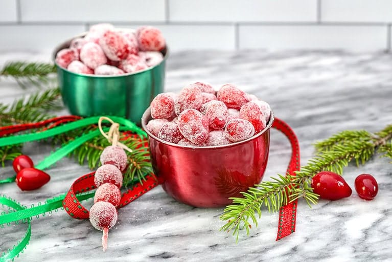 Sugared cranberries in bowls with festive holiday decor.