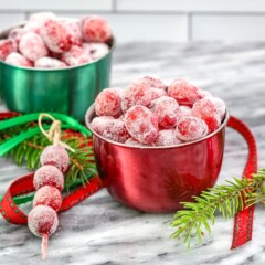 Sugared cranberries in small seasonal bowls and on skewers with festive holiday decorations scattered around them.