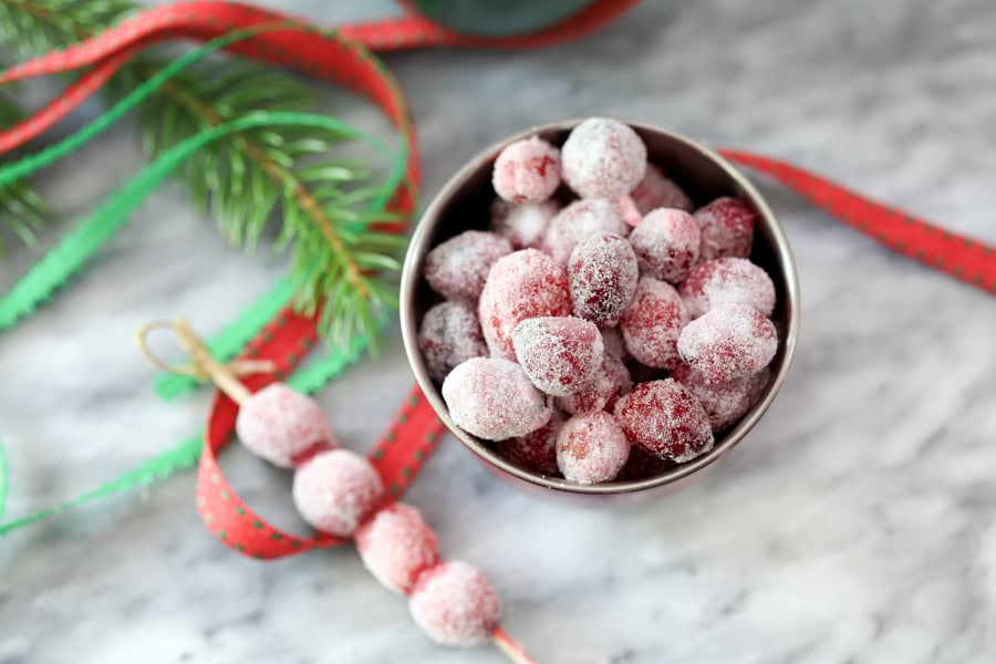 A small bowl and skewer of sugared cranberries with festive decorations around them.