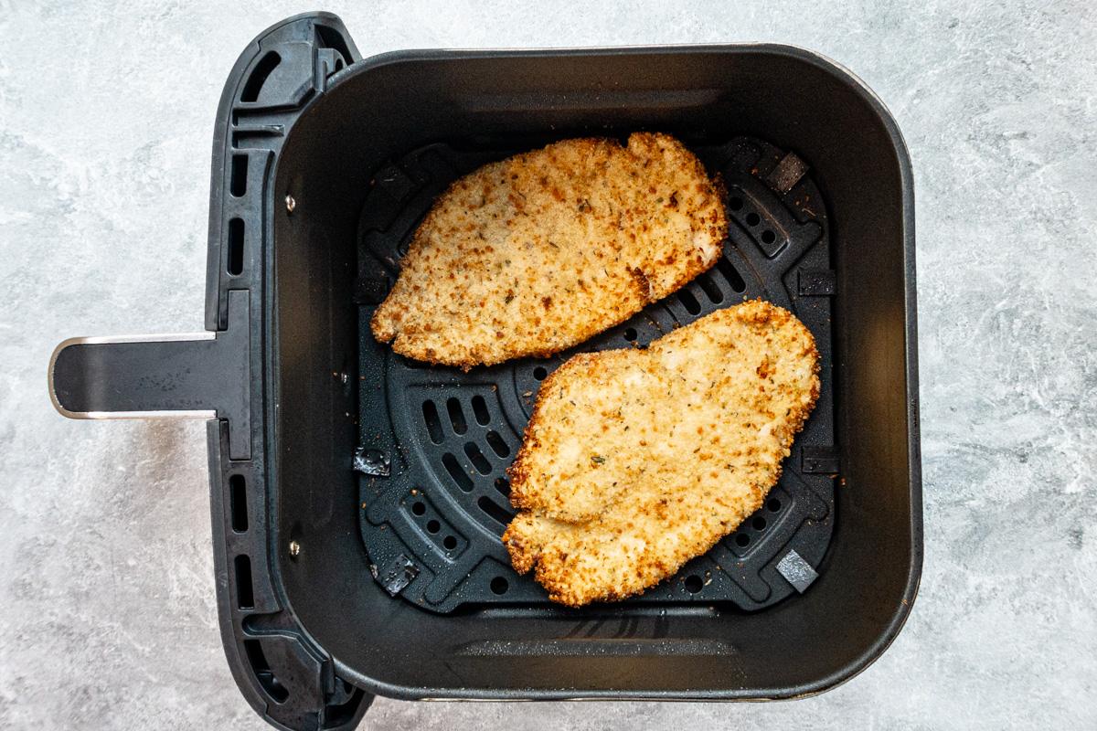 Air fried chicken breast cutlets in the basket, ready to be topped with tomato sauce and cheese.