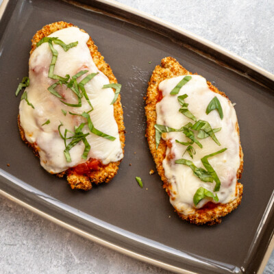 Two air fried chicken breast cutlets topped with tomato marinara sauce, mozzarella cheese, and fresh basil.
