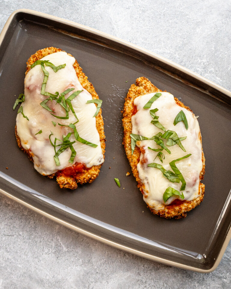 Two air fried chicken breast cutlets topped with tomato marinara sauce, mozzarella cheese, and fresh basil.