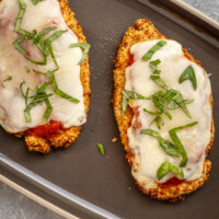 Two air fried chicken breast cutlets topped with tomato marinara sauce, mozzarella cheese, and fresh basil.
