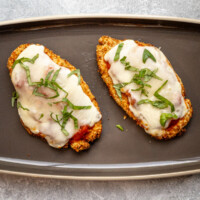Two air fried chicken breast cutlets topped with tomato marinara sauce, mozzarella cheese, and fresh basil.