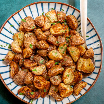 Air fryer potatoes in a decorative serving bowl with serving utensil.