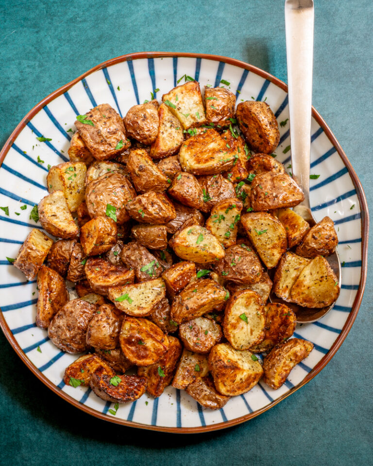 Air fryer potatoes in a decorative serving bowl with serving utensil.