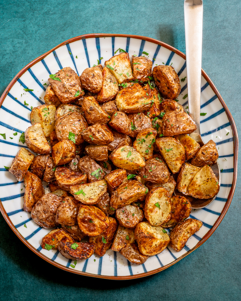 Air fryer potatoes in a decorative serving bowl with serving utensil.