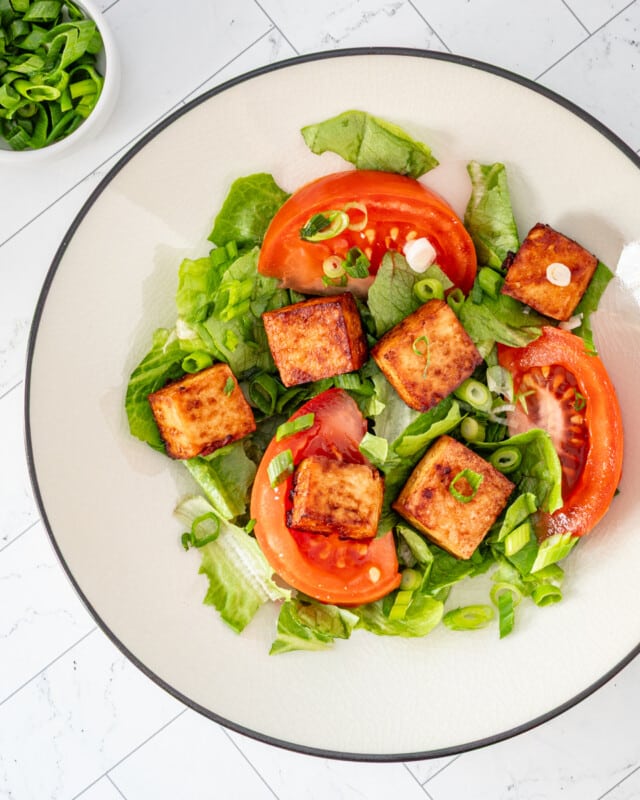 Air fried tofu cubes on lettuce with tomatoes and green onions.
