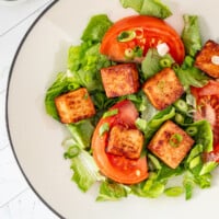 Air fried tofu cubes on lettuce with tomatoes and green onions.