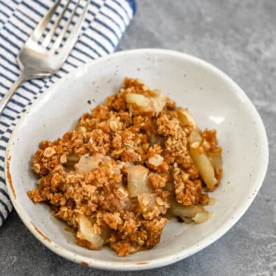 A dessert dish with apple crisp and a fork beside it.
