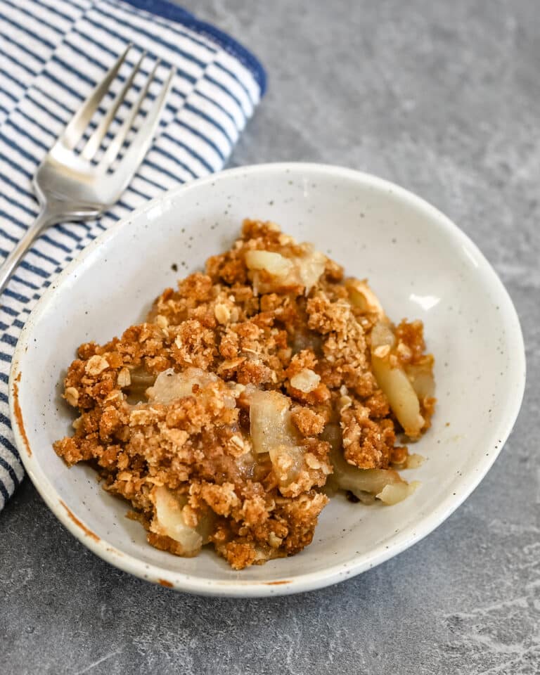 A dessert dish with apple crisp and a fork beside it.
