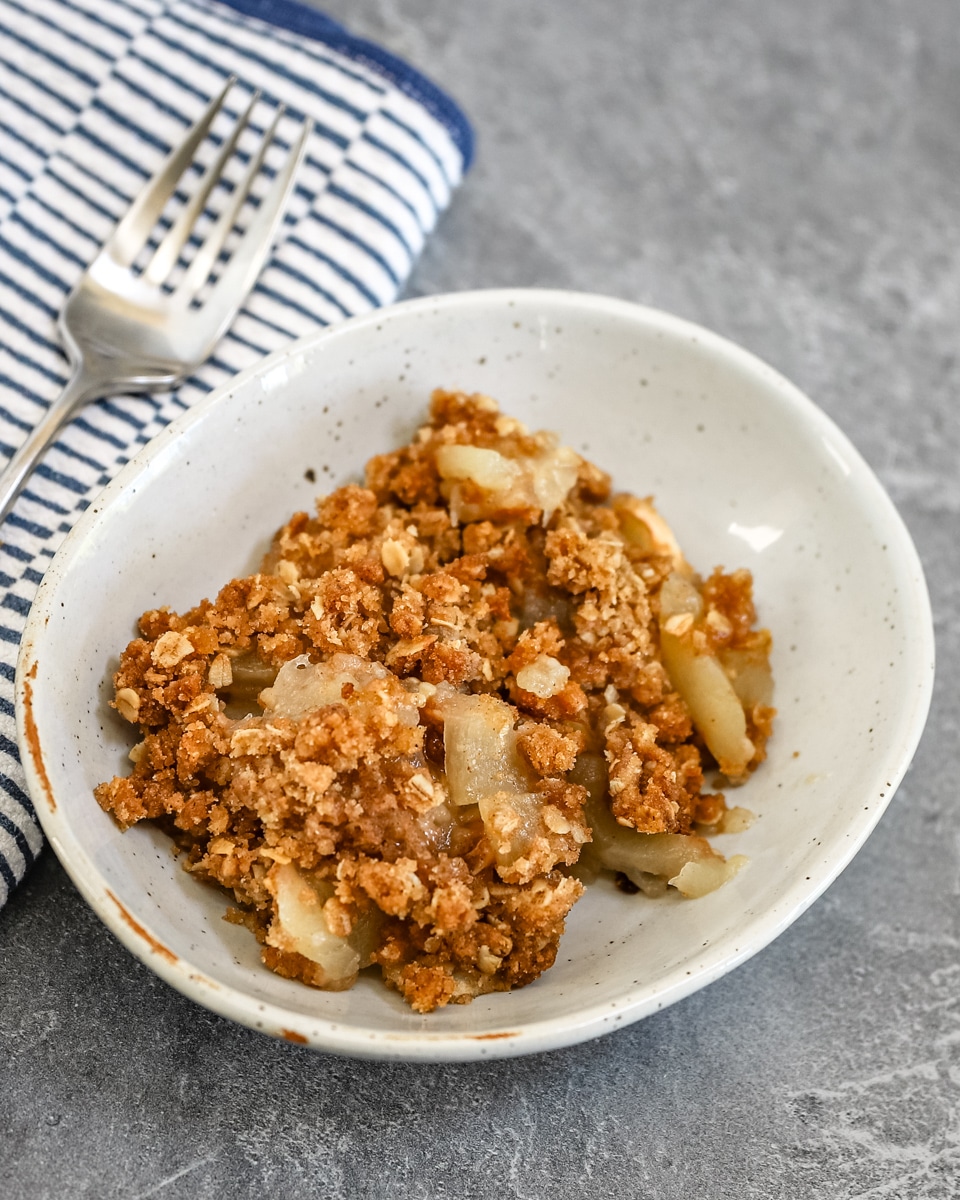 A dessert dish with apple crisp and a fork beside it.