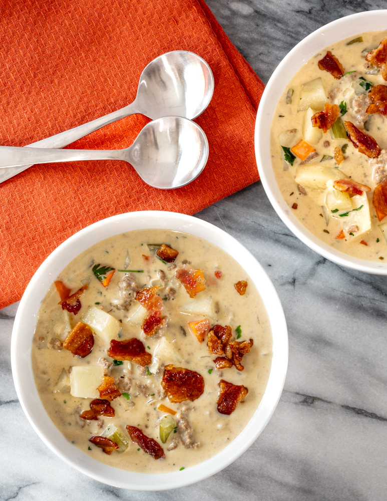 Bacon cheeseburger soup in bowls with an orange napkin.