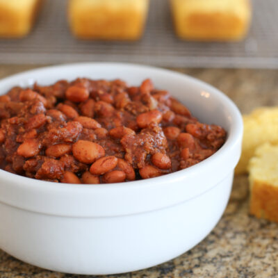 Beefy beans in a bowl with cornbread in the background.