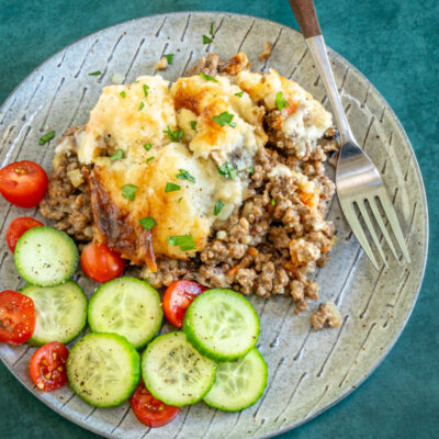 Ground beef casserole with cheesy mashed potato topping and some cucumbers and tomatoes on the side.