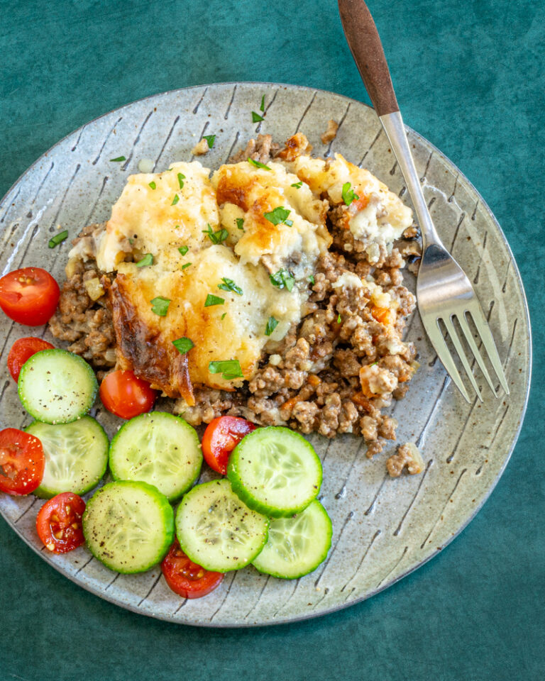 Ground beef casserole with cheesy mashed potato topping and some cucumbers and tomatoes on the side.