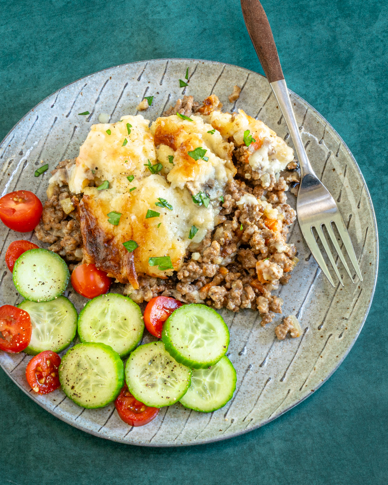 Ground beef casserole with cheesy mashed potato topping and some cucumbers and tomatoes on the side.