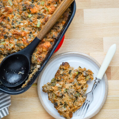 A serving of sausage brioche dressing with the baking dish beside it.