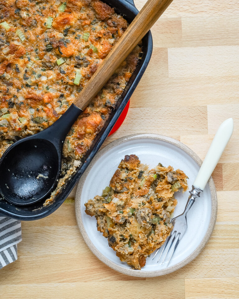 A serving of sausage brioche dressing with the baking dish beside it.