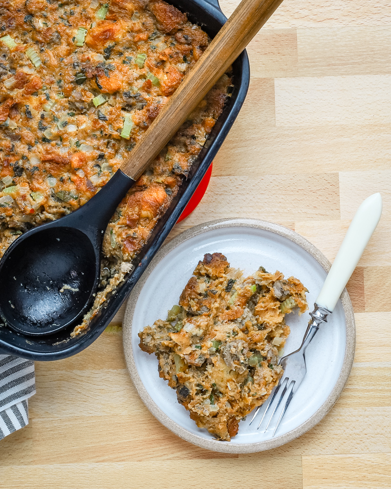 A serving of sausage brioche dressing with the baking dish beside it.