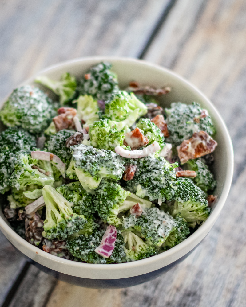Creamy broccoli salad with red onion and bacon bits.