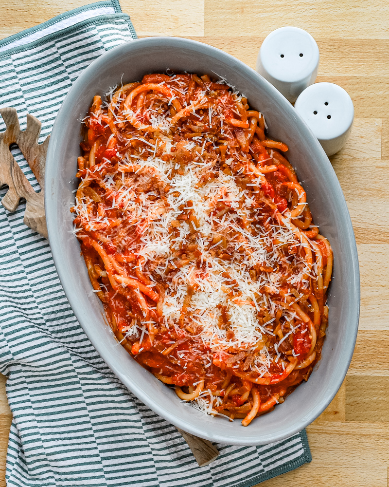 A serving bowl with bucatini all'Amatriciana topped with grated pecorino Romano and extra guanciale.