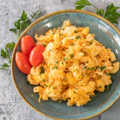 Buffalo chicken mac and cheese on a plate with some parsley and grape tomatoes.