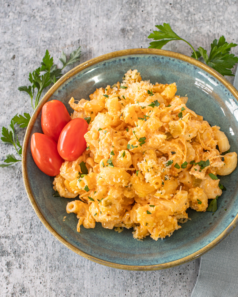 Buffalo chicken mac and cheese on a plate with some parsley and grape tomatoes.