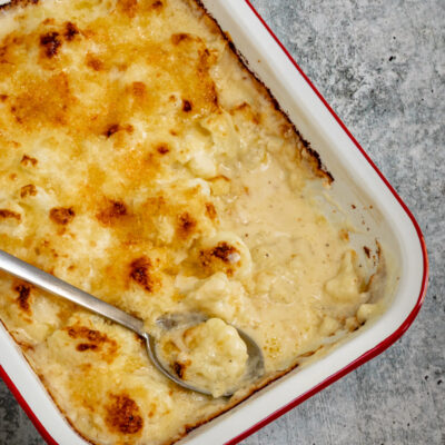 Cauliflower cheese casserole in a baking dish, with serving spoon.