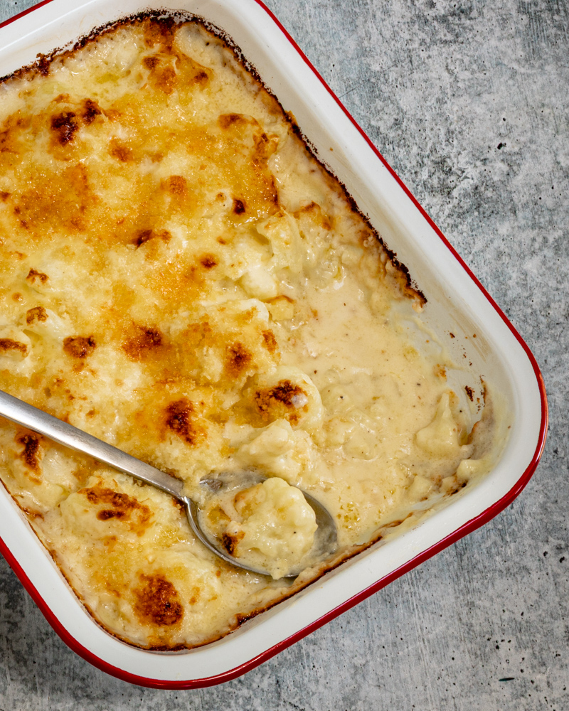 Cauliflower cheese casserole in a baking dish, with serving spoon.