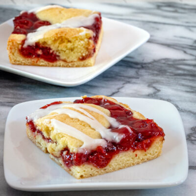 Slices of cherry cobbler bars on dessert plates with a baking sheet alongside them.