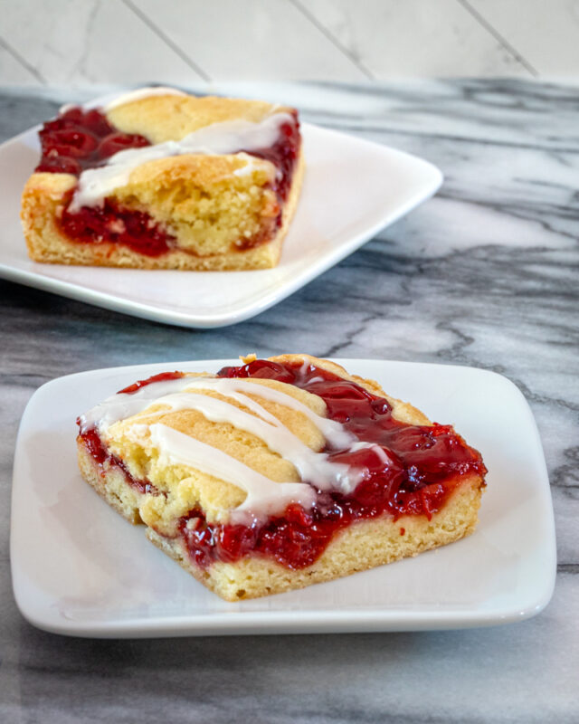 Slices of cherry cobbler bars on dessert plates with a baking sheet alongside them.