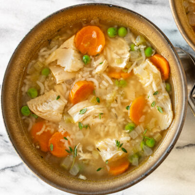 A bowl of chicken and rice soup with carrots and peas.