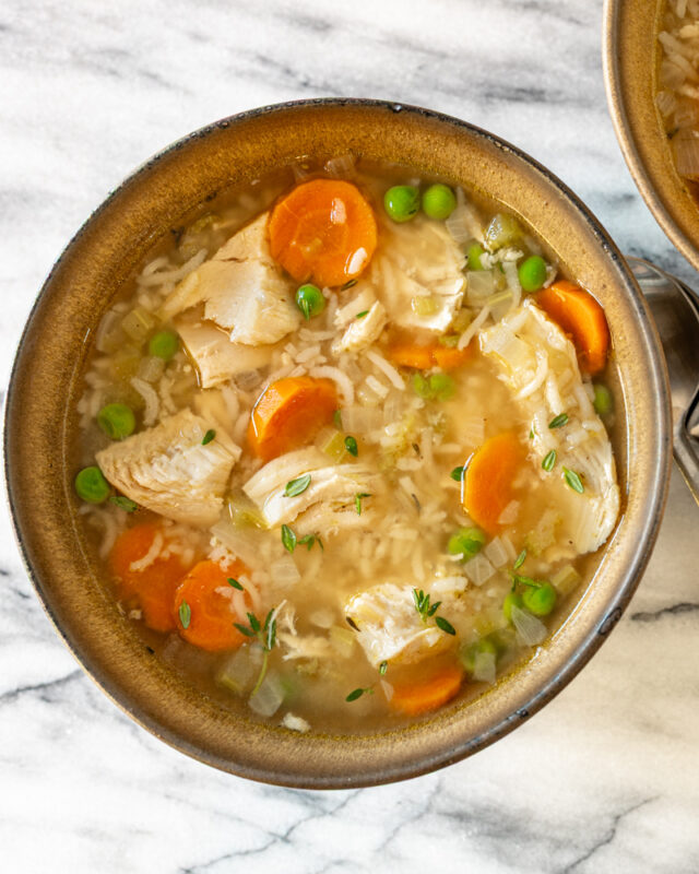 A bowl of chicken and rice soup with carrots and peas.