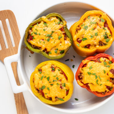 A baking dish with 4 stuffed peppers with cheese topping.