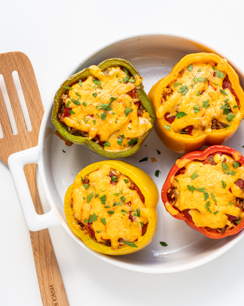 A baking dish with 4 stuffed peppers with cheese topping.
