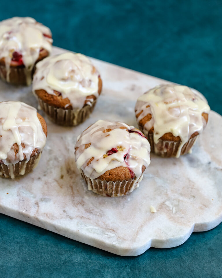 Glazed cranberry orange muffins shown on a marble slab .