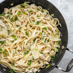 Closeup of creamy chicken pasta with artichokes and green onions.