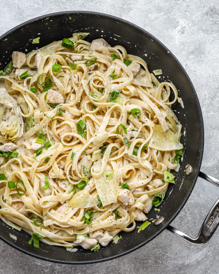 Closeup of creamy chicken pasta with artichokes and green onions.