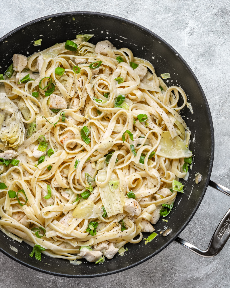 Closeup of creamy chicken pasta with artichokes and green onions.