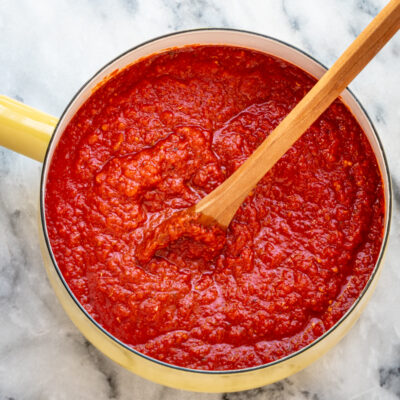 Homemade pizza sauce in a yellow saucepan with a wooden spoon.