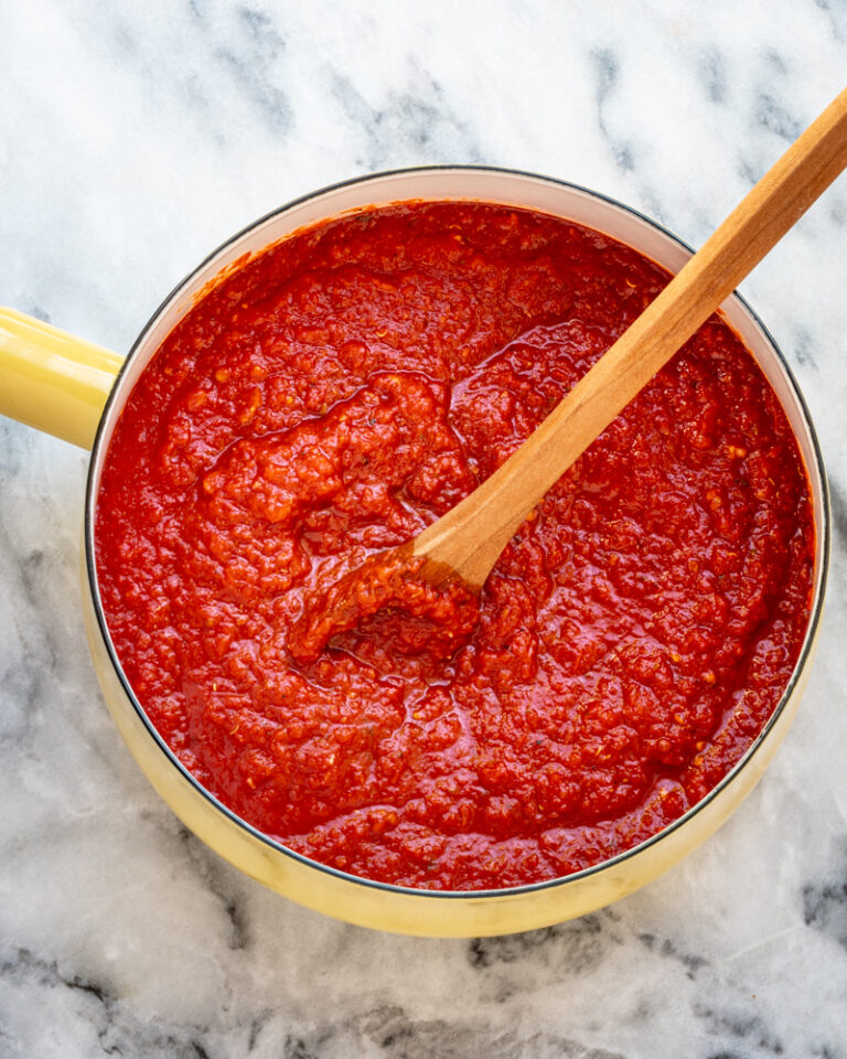 Homemade pizza sauce in a yellow saucepan with a wooden spoon.