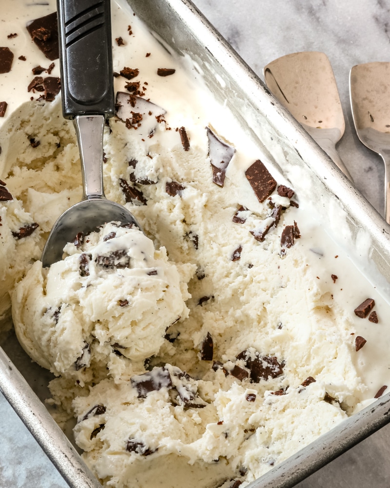 A loaf pan with no churn ice cream being scooped out, and a couple of ice cream spoons on the right.