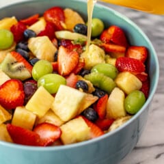 A honey citrus dressing being poured onto a fresh fruit salad in a serving bowl.