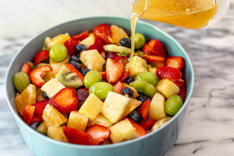 A bowl of fruit salad with dressing being poured over it.