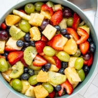 A fresh fruit salad in a large serving bowl with a large serving spoon to the side.